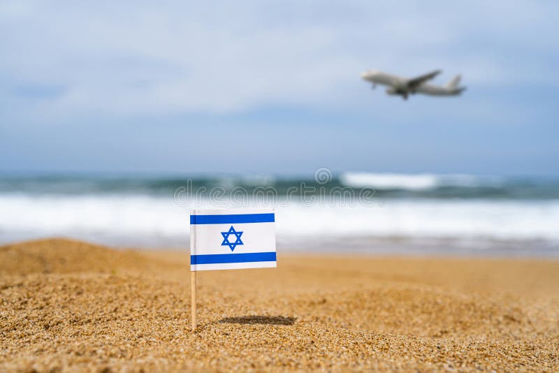 Bandera de israel en forma de palillo de dientes en la arena de la playa frente a la ola del mar con avión de aterrizaje. concepto