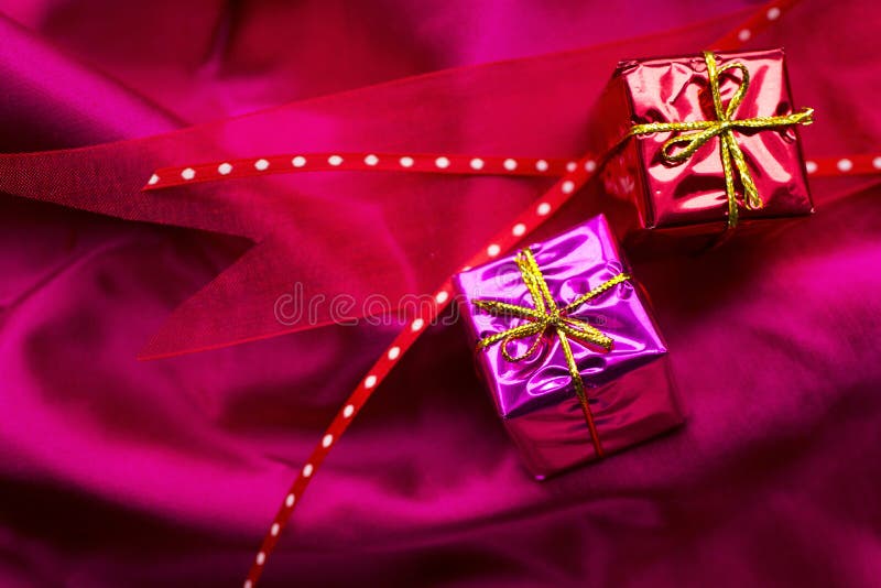 Red ribbon and 2 shinny little gifts on fuschia satin. Red ribbon and 2 shinny little gifts on fuschia satin