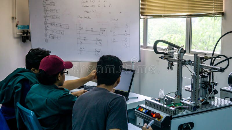 Engineering students discussing and solving the task given on the automation machine system in the laboratory stock image