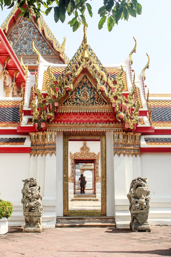 Vertical photo of lion statues guarding doorway to Wat Pho temple, with couple in the distance. Temple of the Reclining Buddha in Bangkok, Thailand. Vertical photo of lion statues guarding doorway to Wat Pho temple, with couple in the distance. Temple of the Reclining Buddha in Bangkok, Thailand.