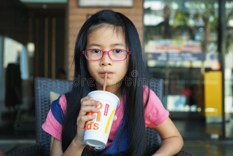 BANGKOK TAJLANDIA, STYCZEŃ, - 19, 2019: mała Azjatycka dziewczyna pił zimnego napój od słomy przed McDonald kawiarnią obrazy stock BANGKOK TAJLANDIA, STYCZEŃ, - 19, 2019: mała Azjatycka dziewczyna pił zimnego napój od słomy przed McDonald kawiarnią obrazy stock