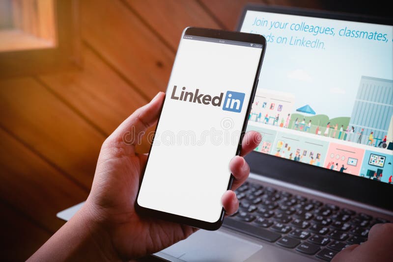 Bangkok, Thailand - August 5, 2019: Hands holding Smartphone with LinkedIn logo on screen and LinkedIn website on laptop