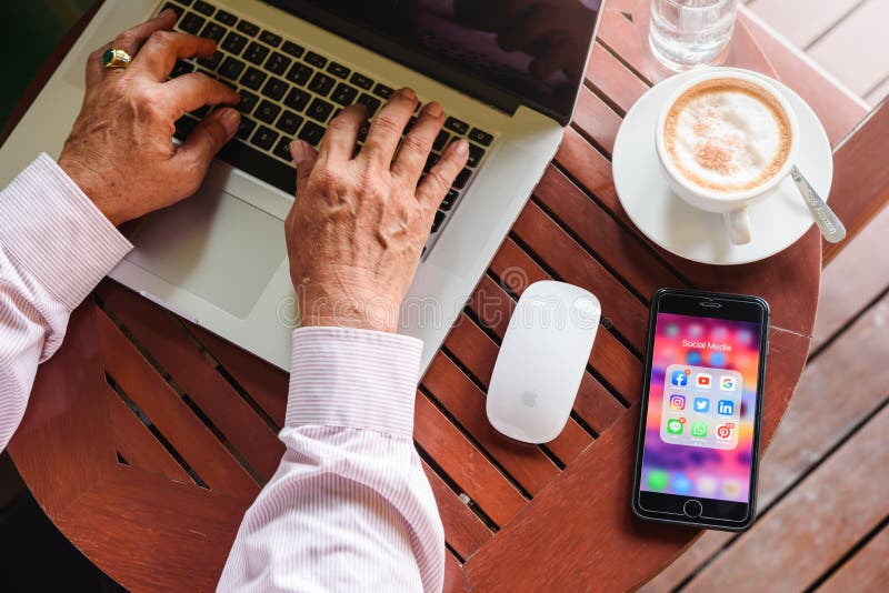 BANGKOK, THAILAND- 23 augusti 2019 : Gamla män arbetar med Macbook pro med Iphone 7 plus med ikonen för sociala medieprogram på royaltyfria foton BANGKOK, THAILAND- 23 augusti 2019 : Gamla män arbetar med Macbook pro med Iphone 7 plus med ikonen för sociala medieprogram på royaltyfria foton