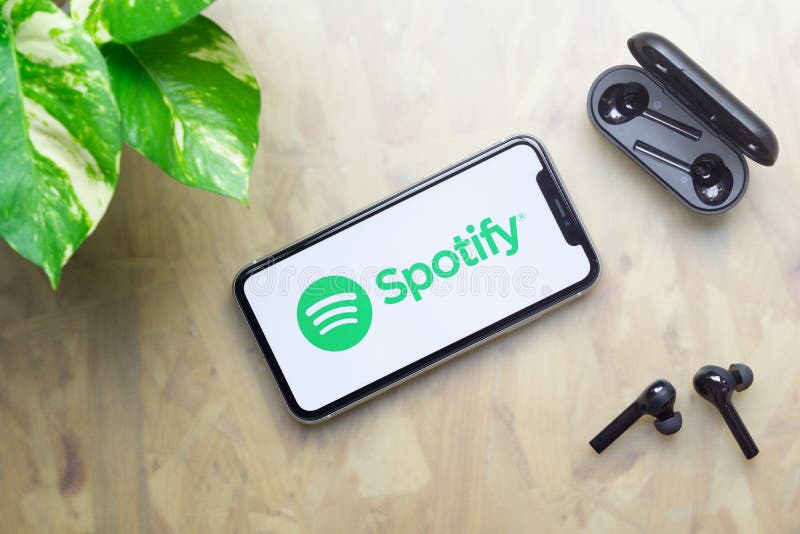 Bangkok, Thailand - July 3, 2020: Apple Iphone 11  with Spotify logo on display, bluetooth headphones with case, green plant on