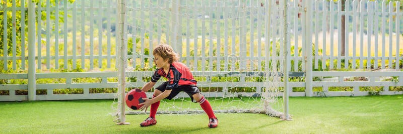 BANNER, LONG FORMAT Little cute kid boy in red football uniform playing soccer, football on field, outdoors. Active