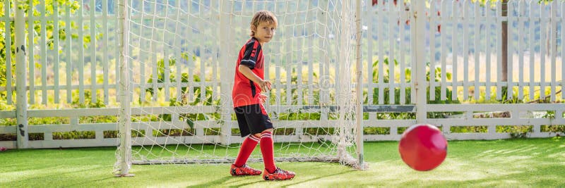 BANNER, LONG FORMAT Little cute kid boy in red football uniform playing soccer, football on field, outdoors. Active