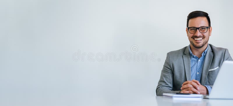 Banner panorama portrait of young smiling cheerful businessman manager entrepreneur with eyeglasses sitting at desk in office or