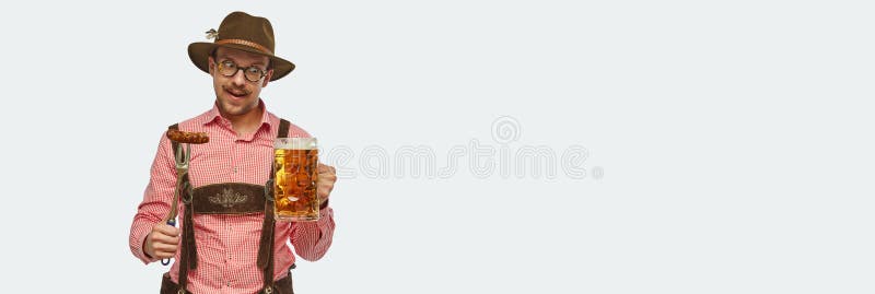 Attractive bavarian man wearing traditional fest outfit holding huge beer mug and appertizing fried sausage. Concept of Oktoberfest, traditions, drinks and food. Banner. Copy space for ad. Attractive bavarian man wearing traditional fest outfit holding huge beer mug and appertizing fried sausage. Concept of Oktoberfest, traditions, drinks and food. Banner. Copy space for ad