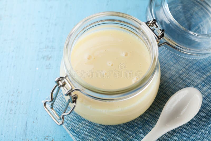 Barattolo di vetro con latte condensato o latte condensato sulla tavola rustica blu immagini stock libere da diritti Barattolo di vetro con latte condensato o latte condensato sulla tavola rustica blu immagini stock libere da diritti