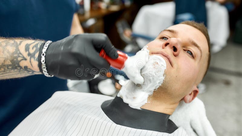 Barba. foto cortada de um barbeiro com braço tatuado, aplicando espuma de barbear com pincel na pele do cliente enquanto imagens de stock royalty free