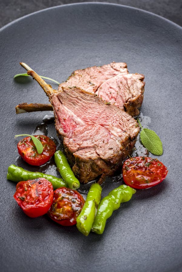 Barbecue rack of lamb neck with paprika and tomato on a modern design plate. Barbecue rack of lamb neck with paprika and tomato offered as close-up on a modern stock photo Barbecue rack of lamb neck with paprika and tomato on a modern design plate. Barbecue rack of lamb neck with paprika and tomato offered as close-up on a modern stock photo