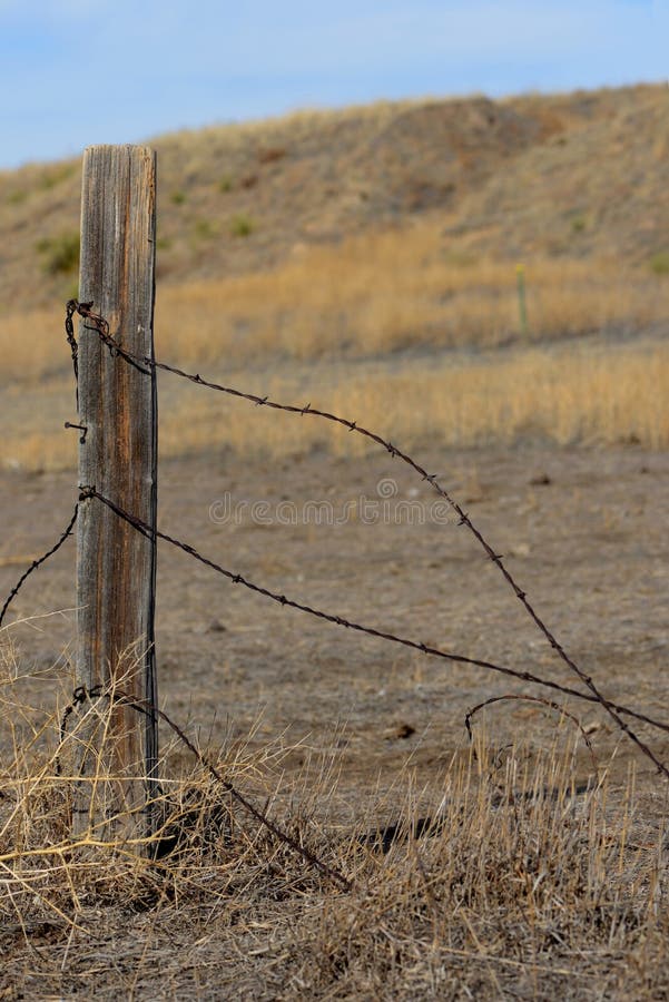 Barbed Wire and Fence Post with Wild Prairie Background