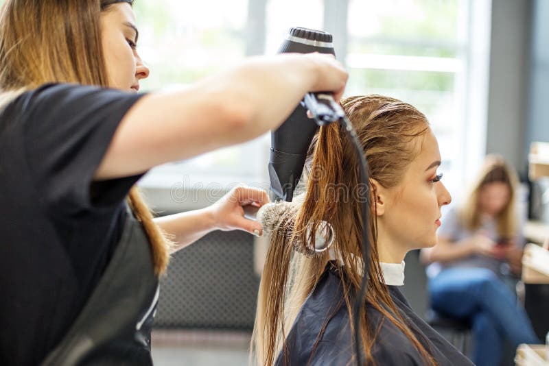 Cabeleireiro seca o cabelo com uma mulher de secador de cabelo no