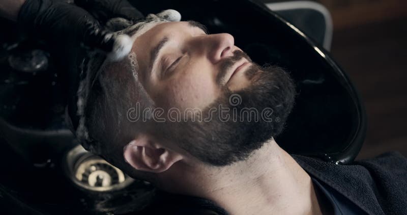 Barber washing head of customer with shampoo