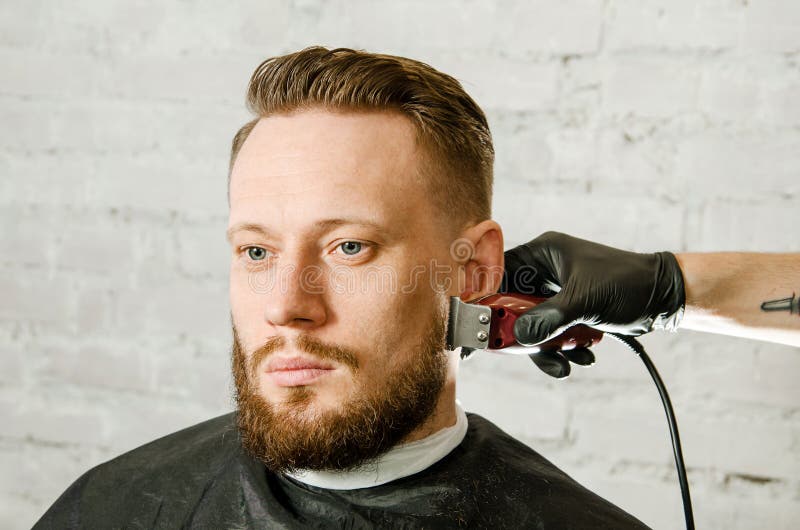 Barberarehanden i handskar klippte h?r och mannen f?r vuxen gihger f?r rakningar den sk?ggiga p? en bakgrund f?r tegelstenv?gg N? royaltyfria bilder Barberarehanden i handskar klippte h?r och mannen f?r vuxen gihger f?r rakningar den sk?ggiga p? en bakgrund f?r tegelstenv?gg N? royaltyfria bilder