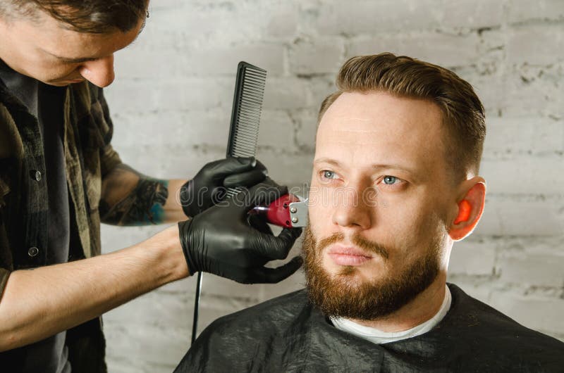 Barberarehanden i handskar klippte h?r och mannen f?r vuxen gihger f?r rakningar den sk?ggiga p? en bakgrund f?r tegelstenv?gg N? arkivfoton Barberarehanden i handskar klippte h?r och mannen f?r vuxen gihger f?r rakningar den sk?ggiga p? en bakgrund f?r tegelstenv?gg N? arkivfoton