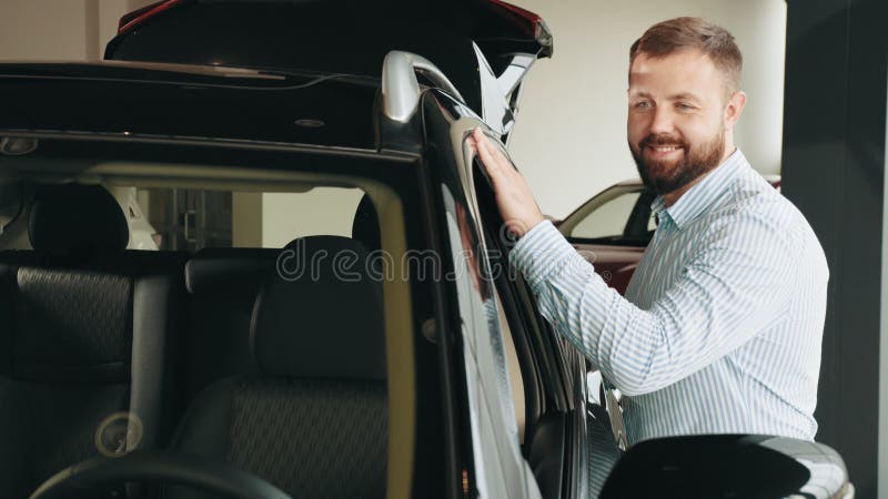 Barbuto con la barba focalizzata che esamina una nuova auto di lusso durante la visita al moderno salone d'esposizione. uomo cauca