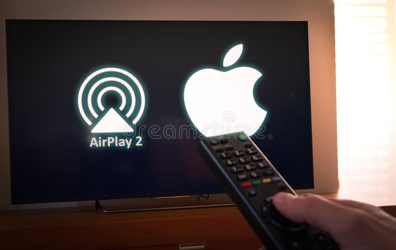 Barcelona, Spain. January 2019: Man holds a remote control With the Apple and Airplay2 icon screen on TV