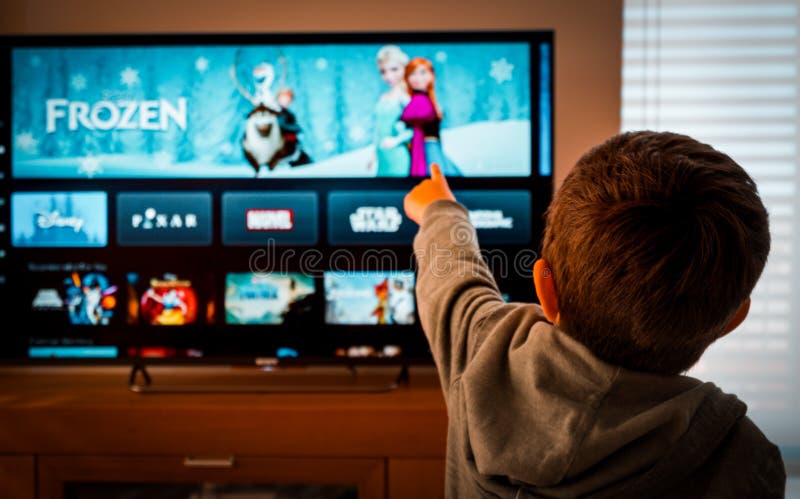Barcelona, Spain. May 2019: Back view image of cute little boy watching the new Disney plus platform on TV