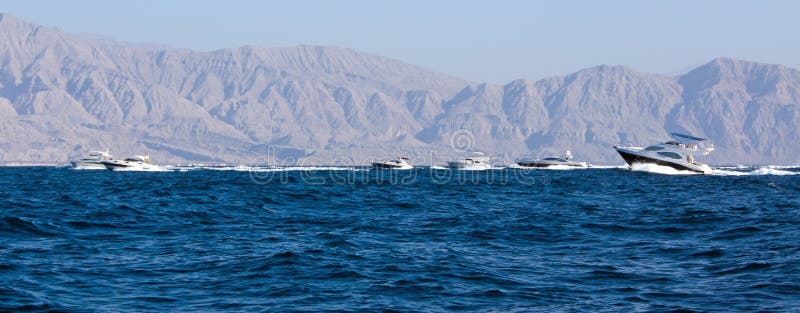 A number of powerful speedboat executive yachts race in the ocean past the Hajar mountains in Ras Al Khaimah, UAE. A number of powerful speedboat executive yachts race in the ocean past the Hajar mountains in Ras Al Khaimah, UAE