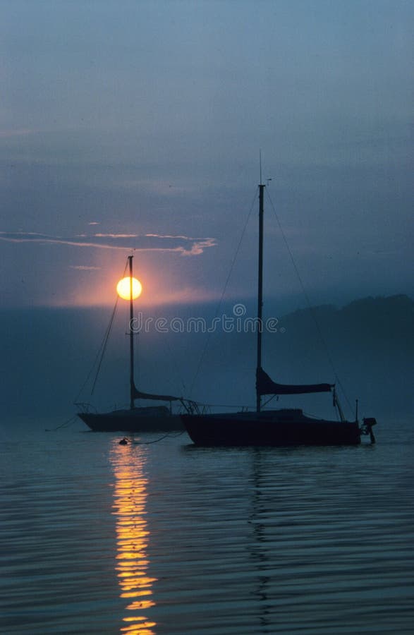 Barcos de vela asegurados en la niebla en la puesta del sol
