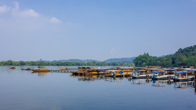 Barcos na doca sobre a água calma do lago ocidental, com os montes na distância, em Hangzhou, China fotos de stock royalty free Barcos na doca sobre a água calma do lago ocidental, com os montes na distância, em Hangzhou, China fotos de stock royalty free