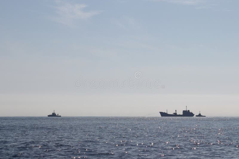 Barcos remolcadores remolcando el barco naufragado Día soleado, mar tranquilo, cielo azul Siluetas de los buques en el horizonte imagen de archivo Barcos remolcadores remolcando el barco naufragado Día soleado, mar tranquilo, cielo azul Siluetas de los buques en el horizonte imagen de archivo