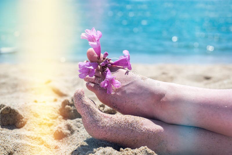 Bare feet on the beach, yellow sand, an exotic flower on the toes of the feet, hot sun, blue sea. Summer and holiday royalty free stock photo Bare feet on the beach, yellow sand, an exotic flower on the toes of the feet, hot sun, blue sea. Summer and holiday royalty free stock photo