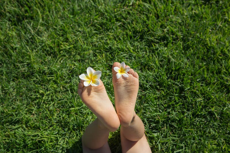 Bare feet of a toddler lying on the green grass. plumeria flowers between baby`s toes