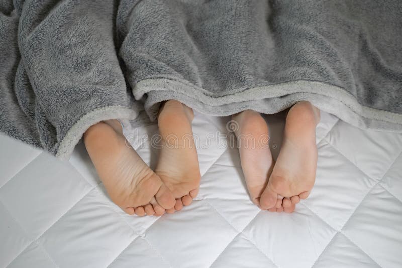 bare feet of two children lying side by side under a blanket on the bed