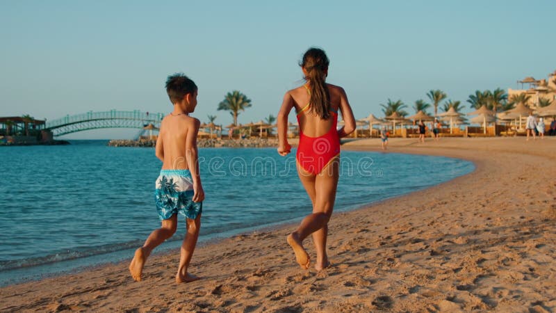 Barefoot children having fun at seashore in sunset. Sibling running on sea beach