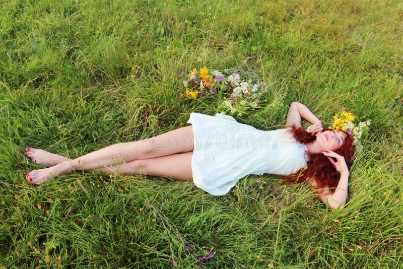 Barefoot girl in wreath lies on grass