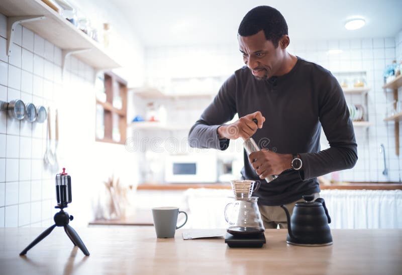 Barista African American man streaming virtual video online of making drip coffee with smartphone at home inside kitchen. Black man sharing professional skills drip coffee for his blog channel. Barista African American man streaming virtual video online of making drip coffee with smartphone at home inside kitchen. Black man sharing professional skills drip coffee for his blog channel