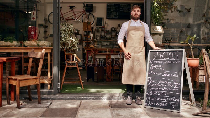 Barista anseende i dörröppningen av en restaurang arkivfoto Barista anseende i dörröppningen av en restaurang arkivfoto