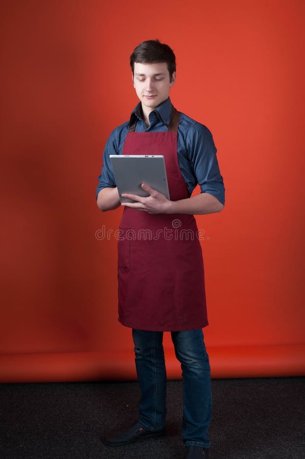 Barista com cabelo escuro no avental de Borgonha que guarda e que olha a tabuleta digital no estúdio da foto fotografia de stock Barista com cabelo escuro no avental de Borgonha que guarda e que olha a tabuleta digital no estúdio da foto fotografia de stock
