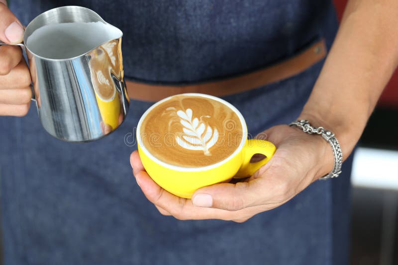 Barista die melkschuim voor het maken van koffie latte kunst met een patroon van de bladeren in een bekertje giet