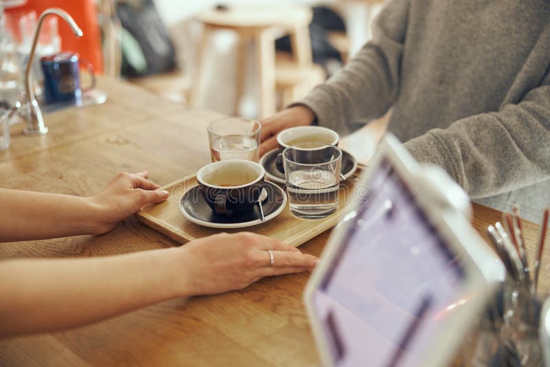 Barista dà ordine al cliente al coffee shop trendy. due tazze di caffè con bicchieri d'acqua.