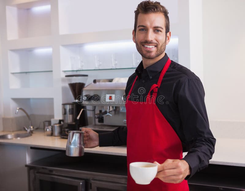 Barista novo considerável que guarda o jarro e a xícara de café fotos de stock Barista novo considerável que guarda o jarro e a xícara de café fotos de stock