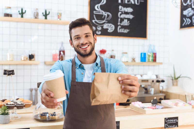 barista novo de sorriso considerável que guarda o café para ir no copo de papel e para levar embora o alimento imagens de stock royalty free barista novo de sorriso considerável que guarda o café para ir no copo de papel e para levar embora o alimento imagens de stock royalty free