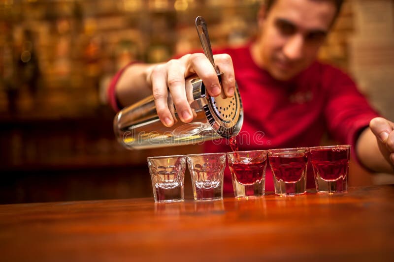 Barman avec le dispositif trembleur de cocktail versant la boisson alcoolisée rouge photo libre de droits Barman avec le dispositif trembleur de cocktail versant la boisson alcoolisée rouge photo libre de droits