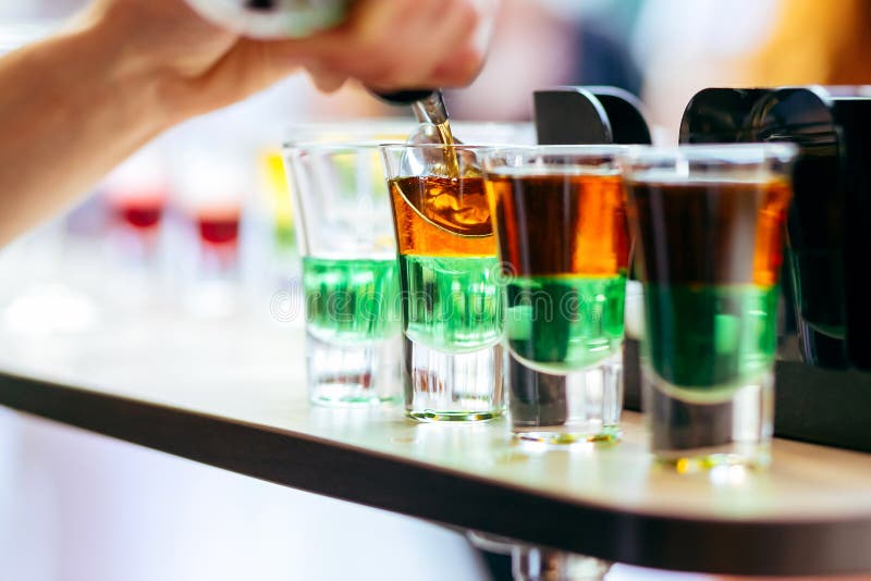 Barman que derrama o cocktail alcoólico em vidros de tiro na barra fotografia de stock Barman que derrama o cocktail alcoólico em vidros de tiro na barra fotografia de stock