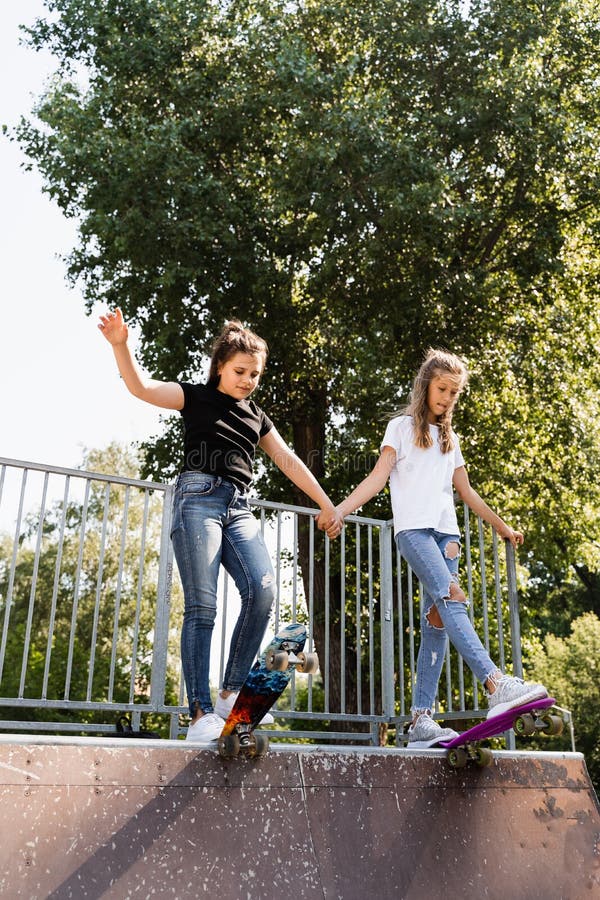 Barn flickor som kissar tillsammans. vänskap. kompisar redo att åka på penny-bord på lekplats för skateboard-parkering. sport arkivfoton