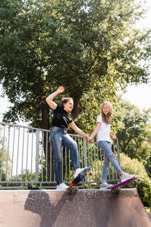 Barn flickor som kissar tillsammans. vänskap. kompisar redo att åka på penny-bord på lekplats för skateboard-parkering. sport arkivfoton
