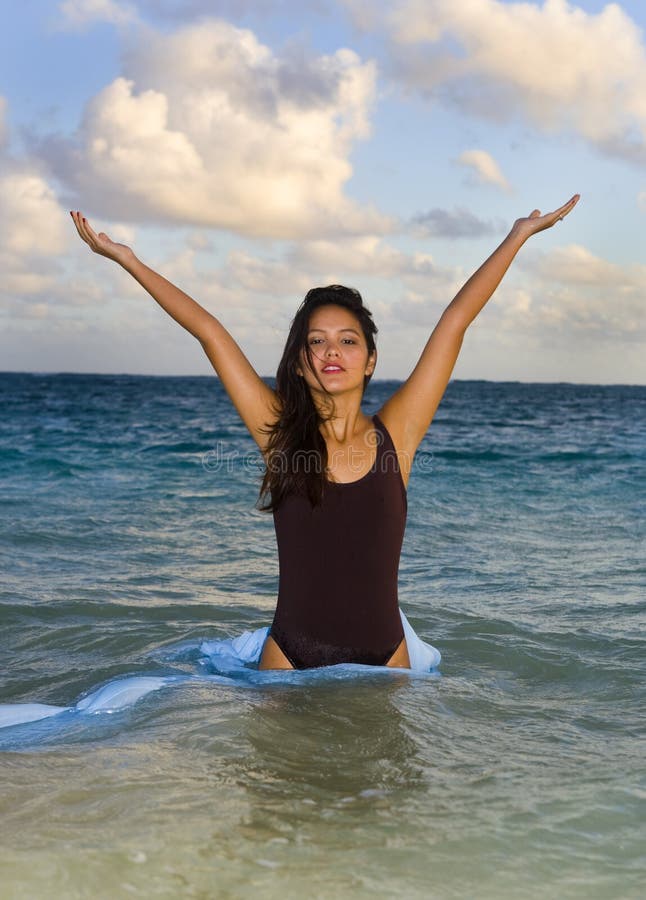 Standing in the warm waters of Hawaii the beautiful young woman lifts her hands to the sky in celebration of finding herself in paradise. Standing in the warm waters of Hawaii the beautiful young woman lifts her hands to the sky in celebration of finding herself in paradise