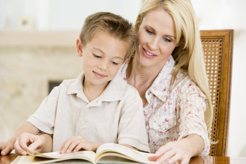 Close up of woman and young boy reading book in dining room smiling. Close up of woman and young boy reading book in dining room smiling