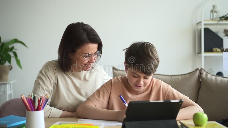 Barn och mor gör läxor med pekplatta spbd. hjälp med att hjälpa pojken att skriva skoluppgift stock video