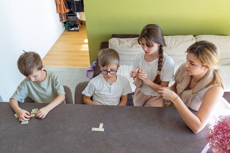 Barn och mor som spelar domino hemma. En mor och tre barn koncentrerar sig medan de spelar domino i hemmet royaltyfri fotografi