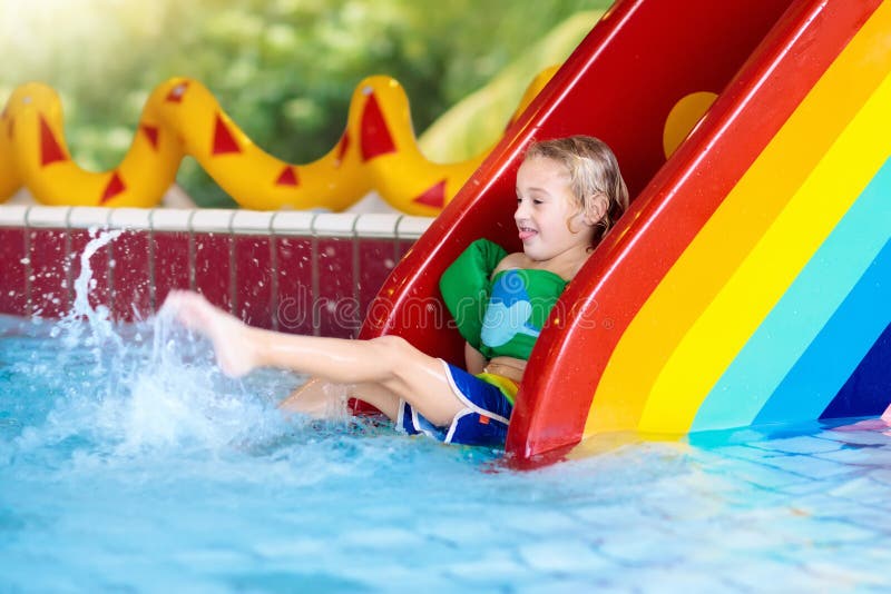 Child on swimming pool slide. Kid having fun sliding in water amusement park. Kids swim. Family summer vacation in tropical resort. Little boy in baby pool with colorful rainbow water slide. Child on swimming pool slide. Kid having fun sliding in water amusement park. Kids swim. Family summer vacation in tropical resort. Little boy in baby pool with colorful rainbow water slide.