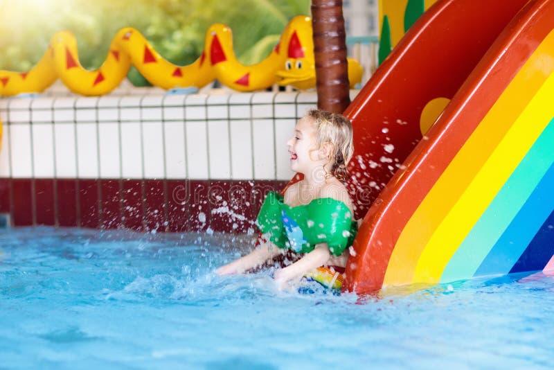 Child on swimming pool slide. Kid having fun sliding in water amusement park. Kids swim. Family summer vacation in tropical resort. Little boy in baby pool with colorful rainbow water slide. Child on swimming pool slide. Kid having fun sliding in water amusement park. Kids swim. Family summer vacation in tropical resort. Little boy in baby pool with colorful rainbow water slide.