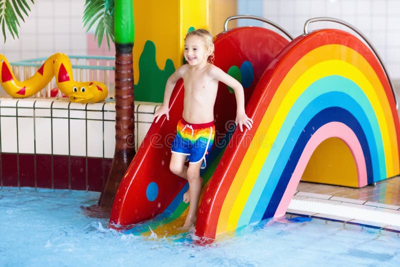 Child on swimming pool slide. Kid having fun sliding in water amusement park. Kids swim. Family summer vacation in tropical resort. Little boy in baby pool with colorful rainbow water slide. Child on swimming pool slide. Kid having fun sliding in water amusement park. Kids swim. Family summer vacation in tropical resort. Little boy in baby pool with colorful rainbow water slide.